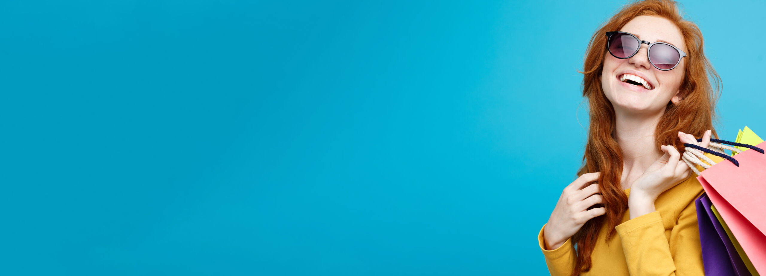 Shopping Concept - Close up Portrait young beautiful attractive redhair girl smiling looking at camera with shopping bag. Blue Pastel Background. Copy space